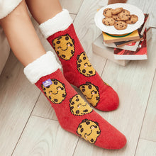 Load image into Gallery viewer, The Foozie™ Cookie Red slipper socks, smiling cookie print on red, worn on a wooden floor beside a plate of cookies