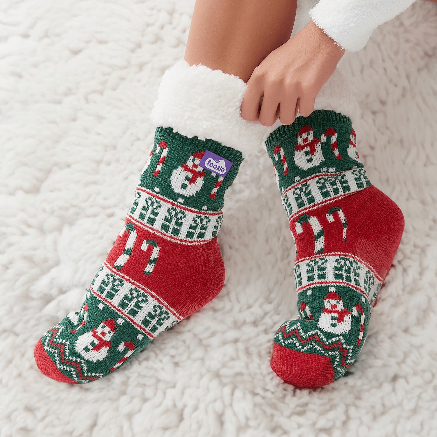 The Foozie™ Christmas Snowman slipper socks, hands pulling up the sherpa cuff on a fluffy white rug