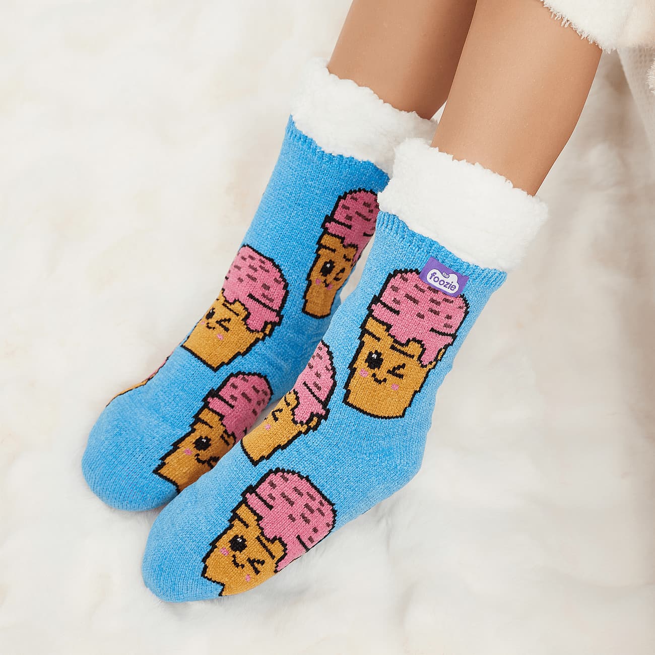 The Foozie™ Ice Cream slipper socks, smiling ice cream cone print on blue, worn on a fluffy white rug